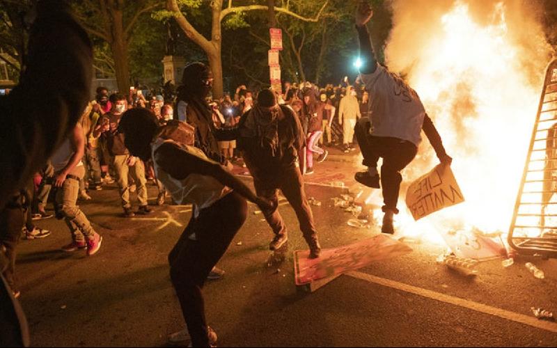 Protesters jump on a street sign near a burning barricade during a demonstration against the death of George Floyd. AFP