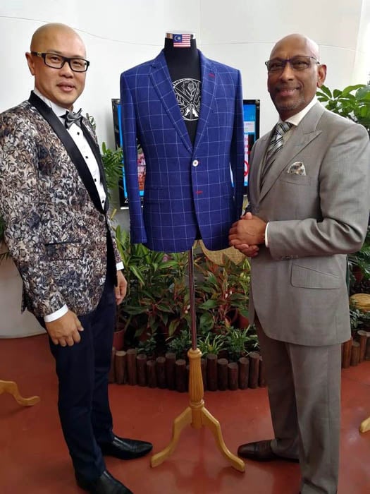 黄荻耀与伦敦萨维尔街著名的Maurice Sedwell首席裁缝兼总经理安德鲁，在台湾2017年世界洋服同业联盟第37届年会参展的OZ Homme亚盟西装裁剪赛冠军作品旁合照。