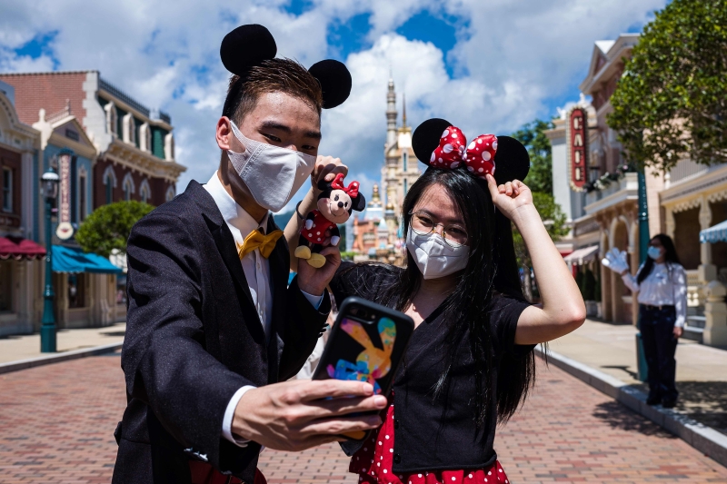 一对男女在香港迪士尼乐园前自拍，香港迪士尼乐园在关闭5个月后重新开放。游客都自觉地带口罩。