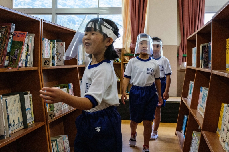 疫情新常态，木县日光市鬼怒川小学的小学生们带上防护头罩在图书馆找书。（图：法新社）