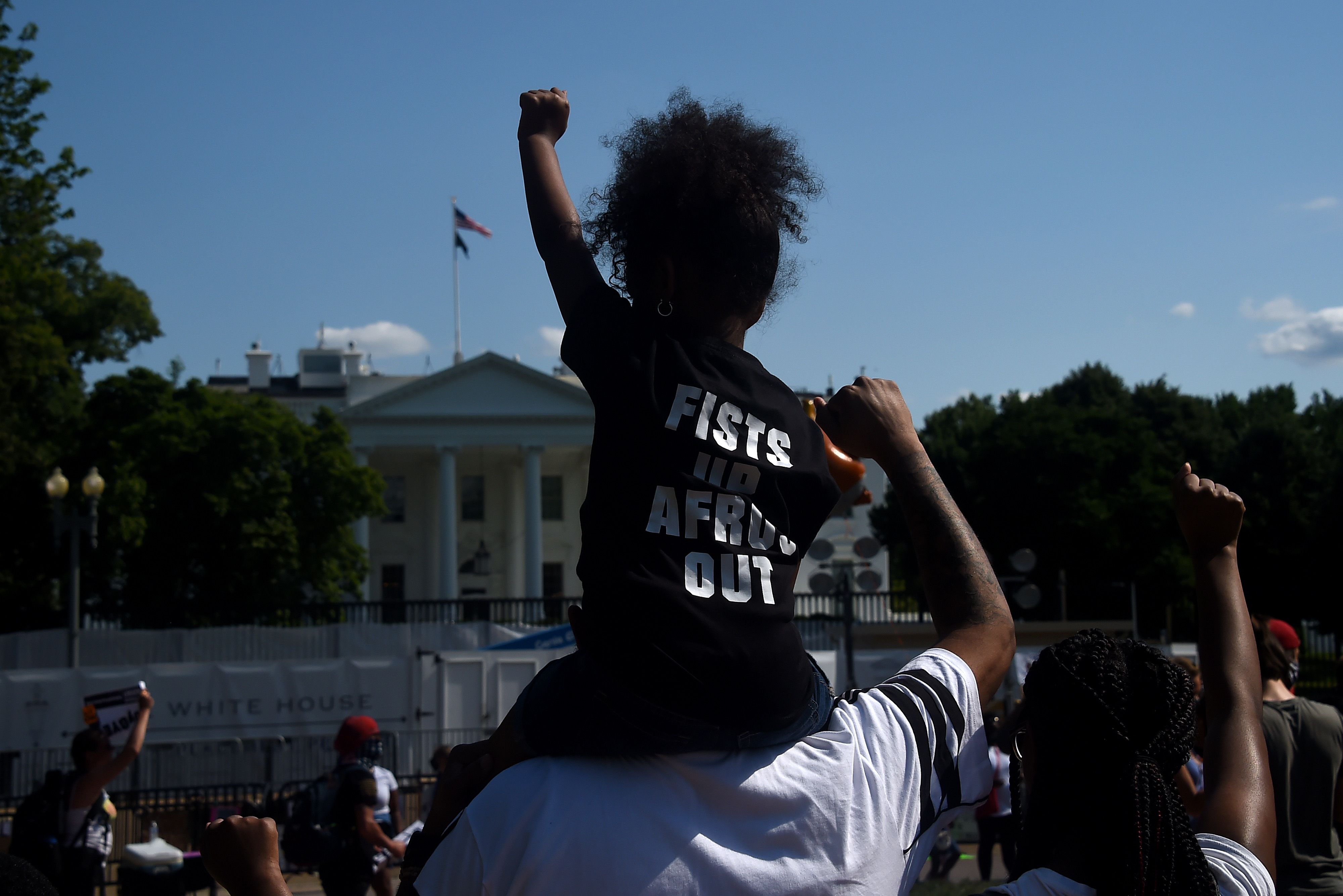 一名非裔男童跨坐大人的肩膀，向白宫举拳抗议。（图：法新社）