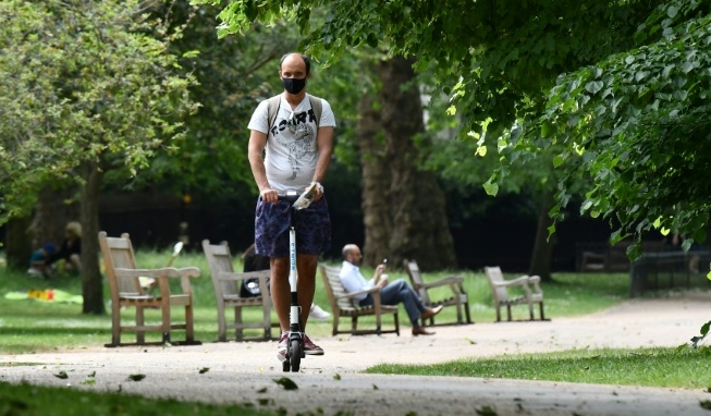 A man wears a face mask as he scooters through St James's Park in central London as lockdown measures are eased. AFP