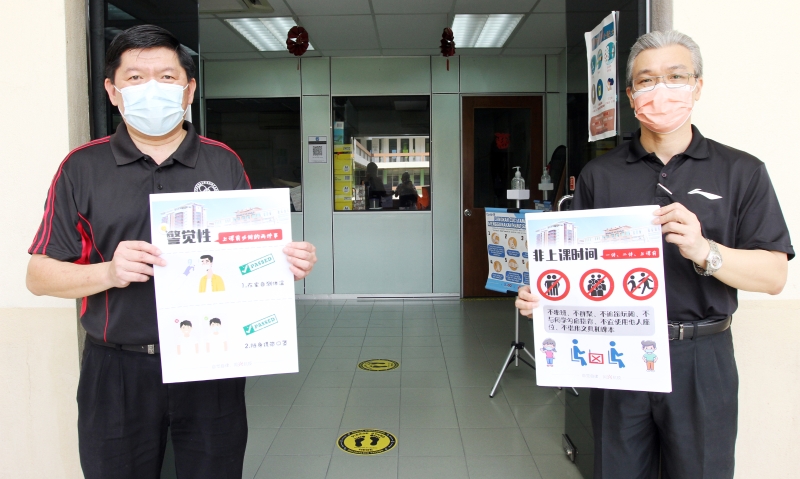 苏进存（左起）和副校长李荣兴向记者展示将在学校各角落张贴防疫措施的海报。