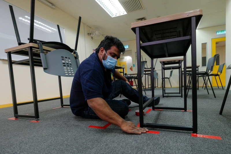 吉隆坡圣约翰中学校工在地上贴上胶布划分桌椅距离（马新社图）