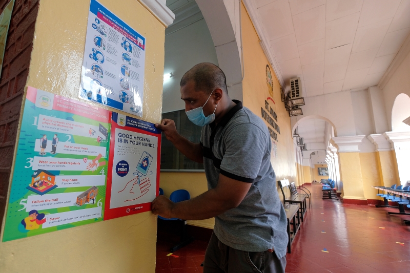 吉隆坡圣约翰中学校工张贴海报，确保遵守安全及卫生指南。