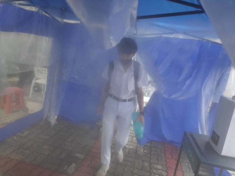 新文龙中华中学学生在消毒帐棚内进行喷雾消毒。