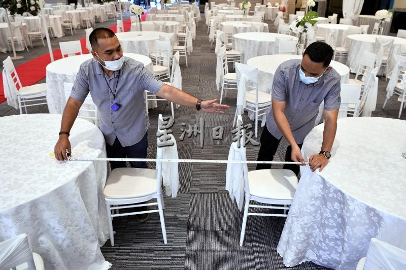 2名工作人员正在检测餐桌之间的距离，确保遵守标准作业程序。
