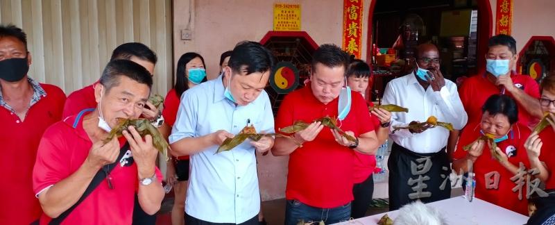 粽子是端午节的应节食品，谢琪清（前排左二）获得拉杭新村盂兰盆会赠送粽子，并与大伙儿吃起来，津津有味。（图：星洲日报）