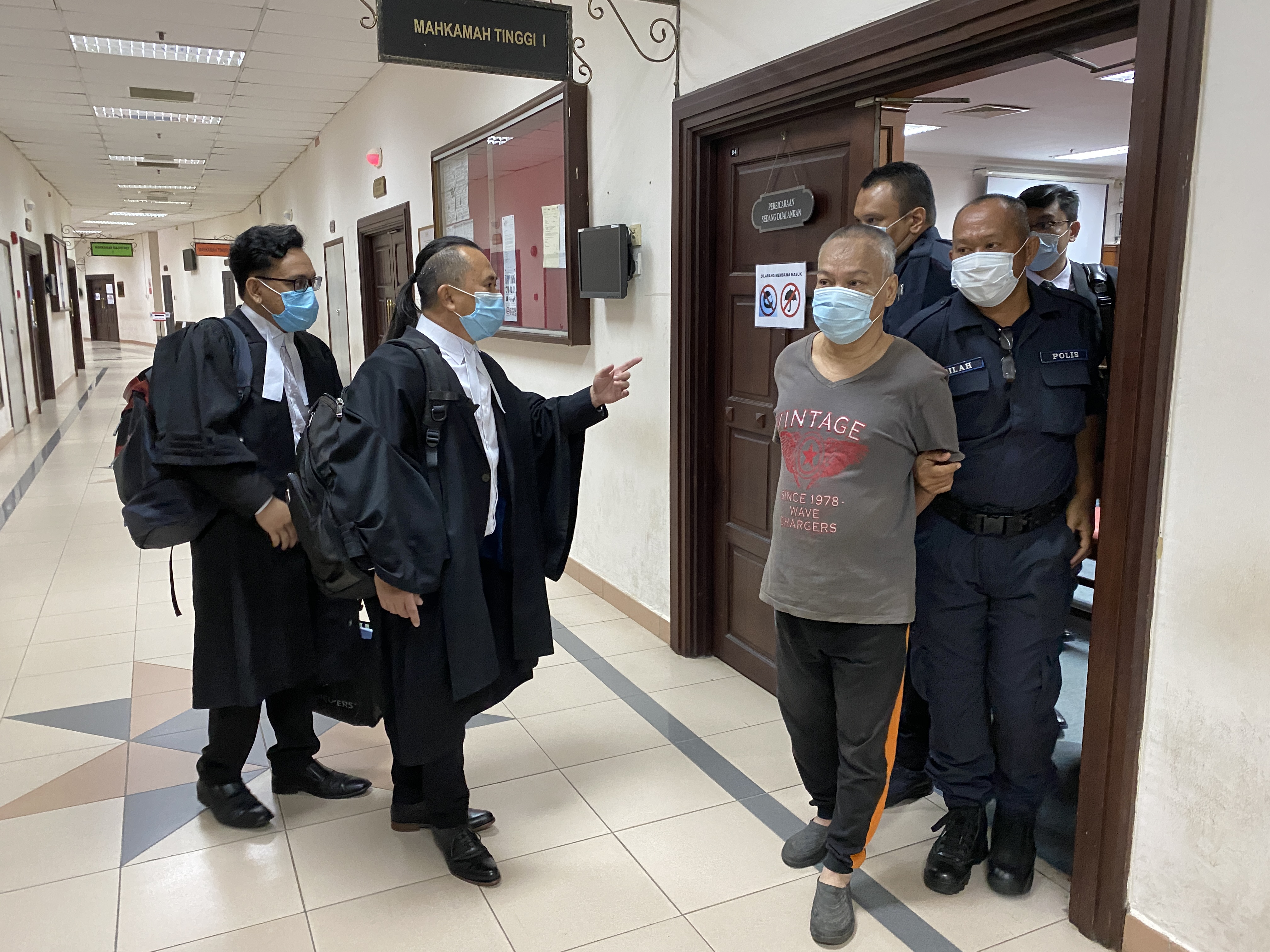 被告班丹兰谷（前排右二）被押出法庭时，其辩护律师向他解释，虽然没有被判死刑，但必须进入精神病院接受治疗。

