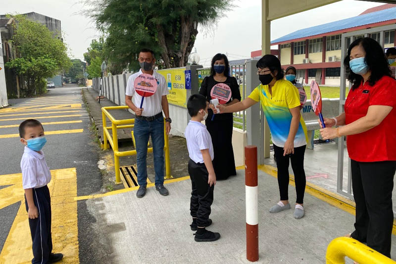 老师在为学生测量体温的同时，杨式丰（左一）、校长及副校长也高举写上“开学了，欢迎你”的牌子，欢迎孩子们返回校园。