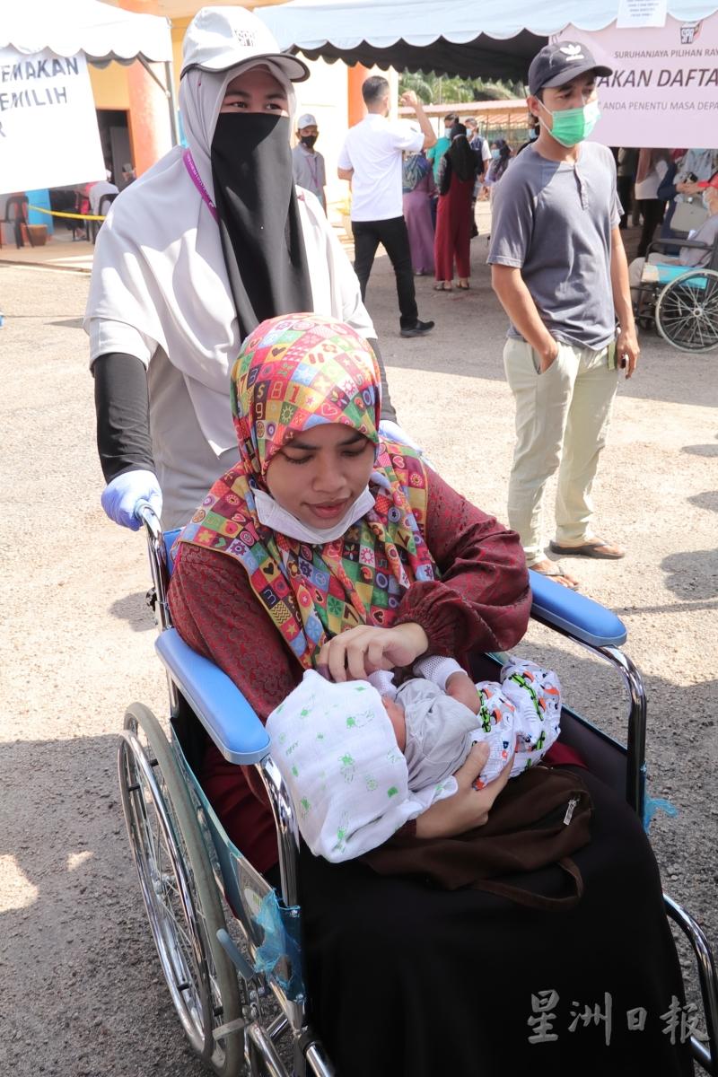 一名初产的马来妇女抱著襁褓中的婴儿，坐上轮椅来到投票中心，履行投票义务。