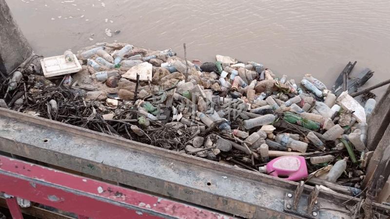 木柴、塑胶瓶等垃圾堆积在水闸门，若没及时清理，全部会被冲到河道下游。