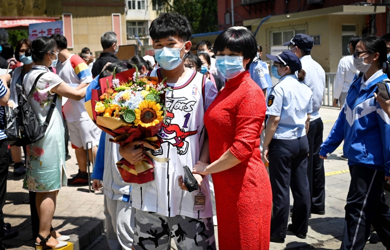 一名戴着口罩拿著一束鲜花的学生与他的父母在学校门口合影。
