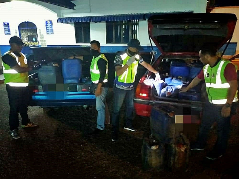 贸消局执法人员展示被充公的2辆轿车及用于走私的桶装汽油。