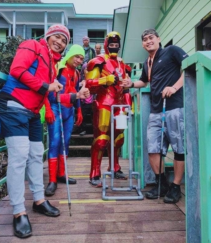“钢铁人”约翰查尔斯（右二）把无腿男法兰西制作的PVC脚踏式消毒搓手液架送到拉班拉达半山旅舍。