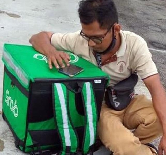 Fazah sits by the roadside with the Grab delivery bag after losing his motorbike. Fazah sits by the roadside with the Grab delivery bag after losing his motorbike.