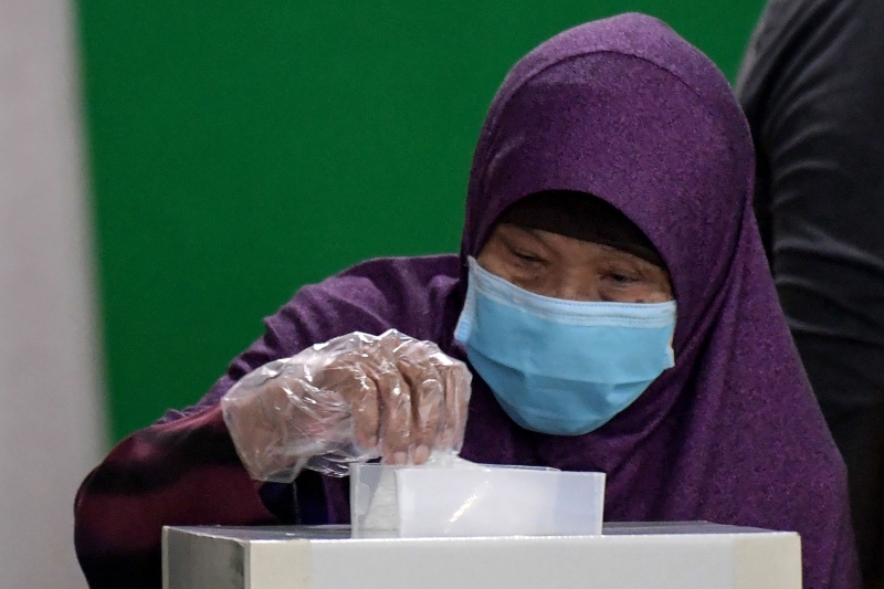 一名戴著口罩的女选民投下她手中的一票。