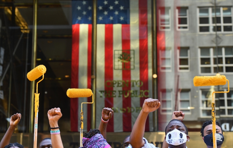 参与涂鸦者在美国国旗前高举黄色油漆滚轮和他们的拳头，为种族平等发声。