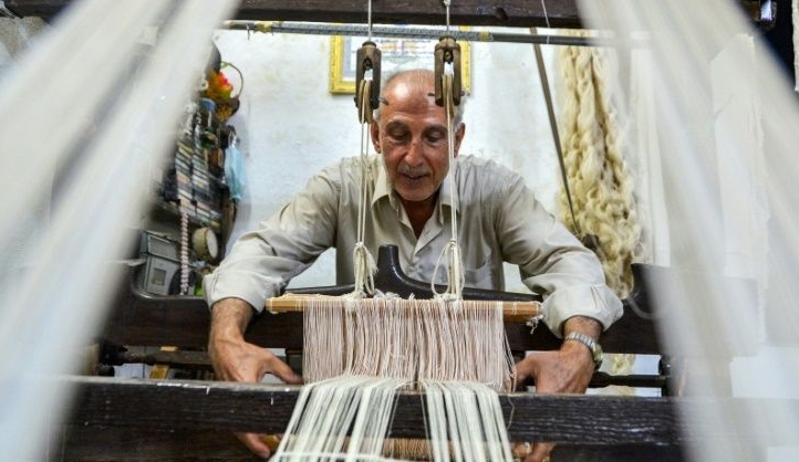 Muhammad Saud hand weaves silk threads on a loom at his home workshop in Deir Mama. AFP