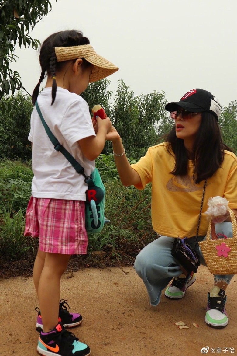 章子怡毫无偶像包袱，蹲在路边就开始吃桃子了，将剥好的桃子小心翼翼地递给女儿。