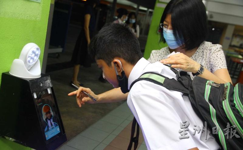吉隆坡冼都中文华小学生在老师的引导下，通过电子仪器检测体温。