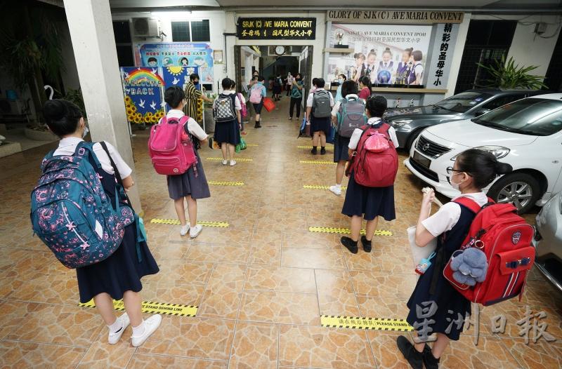 学生背着笨重的书包，乖巧站在黄色的线条上，与小伙伴维持社交距离。
