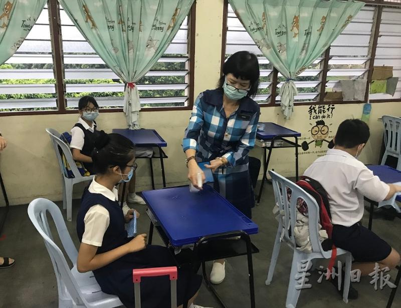 校长杨金春在学生桌子上喷射清洁剂，学生过后使用纸抹布抹干净桌子。