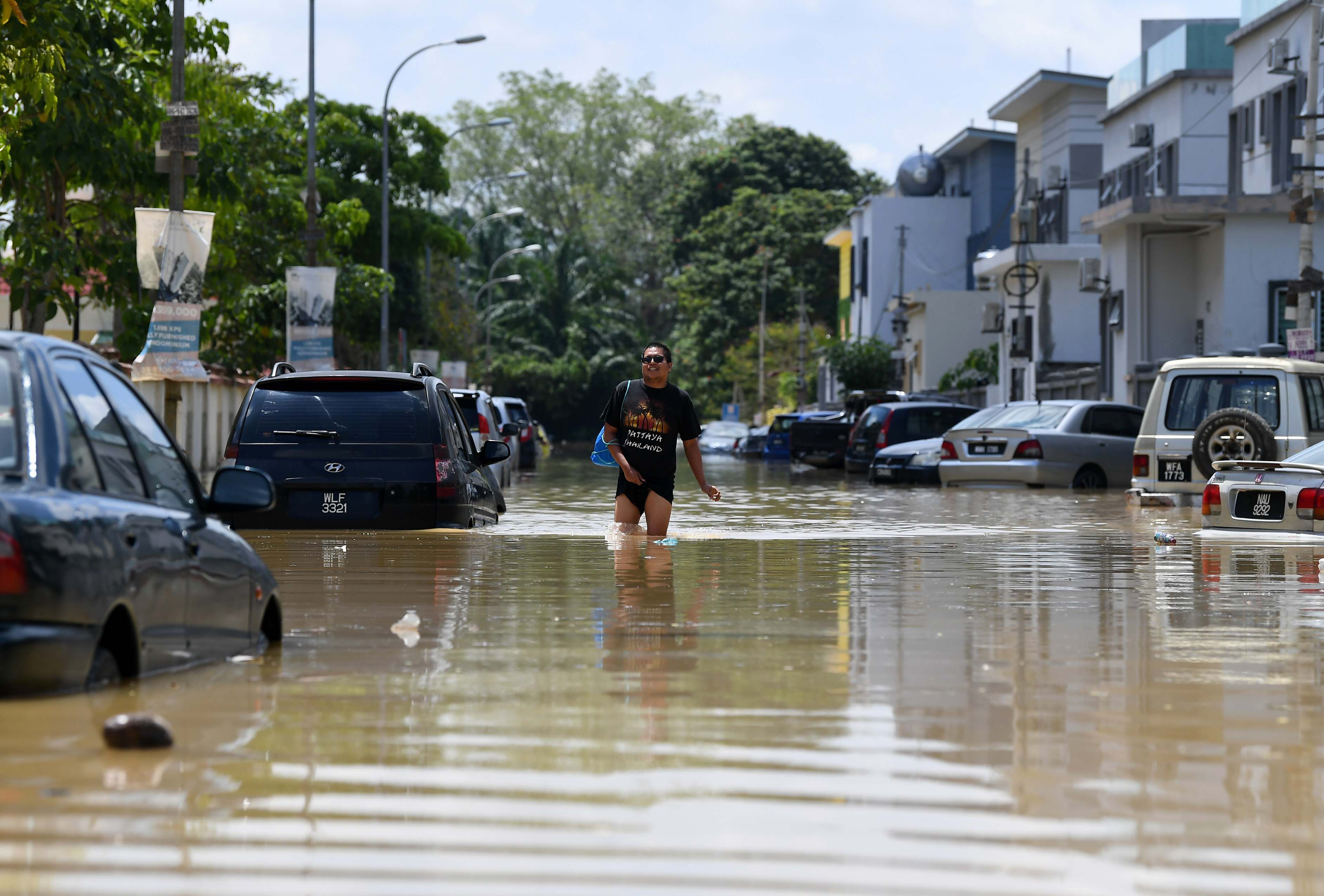 一名居住在龙溪Kristal花园的居民拉高裤脚慢行在自家外水灾的马路上。（马新社图）