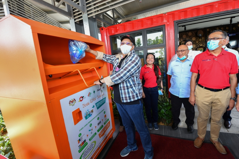 安努亚慕沙（左）为“革新回收设施”（FIKS）主持开幕，并示范将可回收废物放入“S@S”奖励系统的回收箱内。