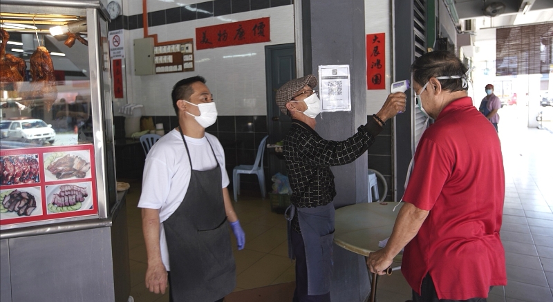 王志兴（左）陪同员工在进入口处为顾客测量体温。