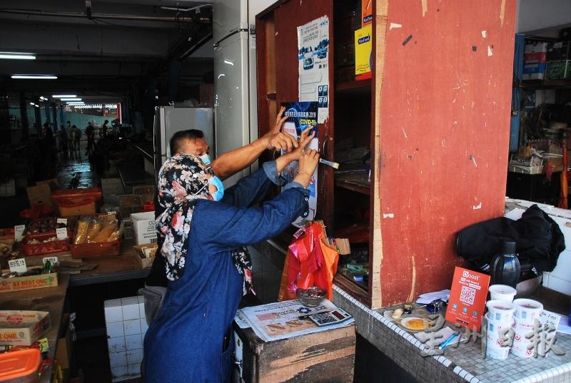 官员协助小贩将防疫海报贴到橱上。