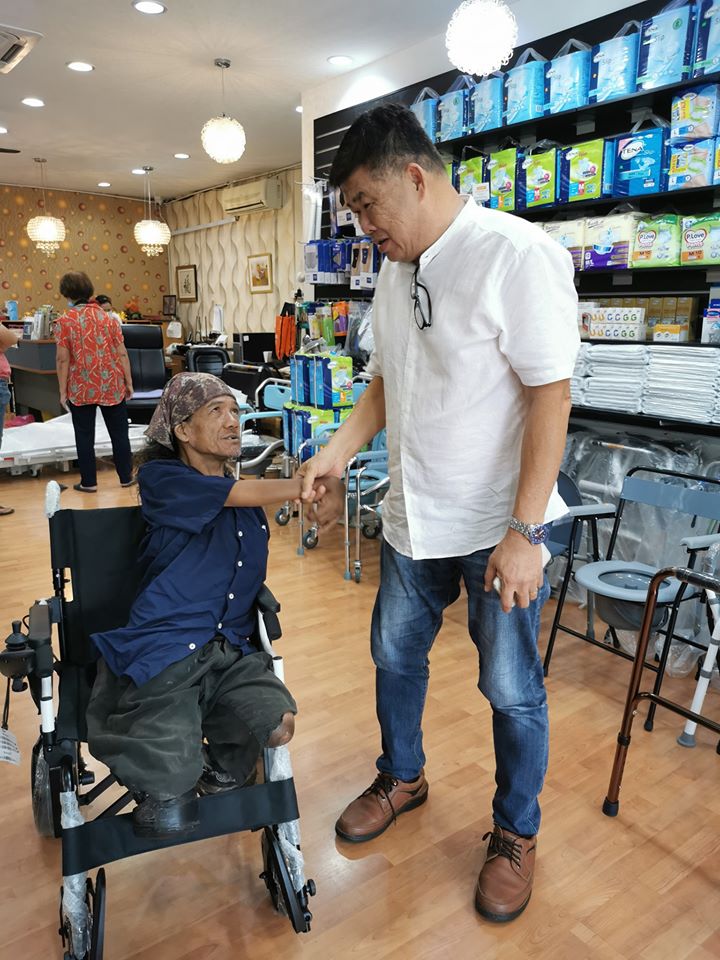 达乌德（左）坐在他期盼多年的电动轮椅上，与关志庭握手表示感谢。