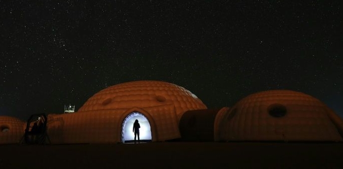 A member of the AMADEE-18 Mars simulation mission wearing a spacesuit standing in the doorway of a simulation habitat, with a view of the night sky above in Oman's Dhofar desert. AFP