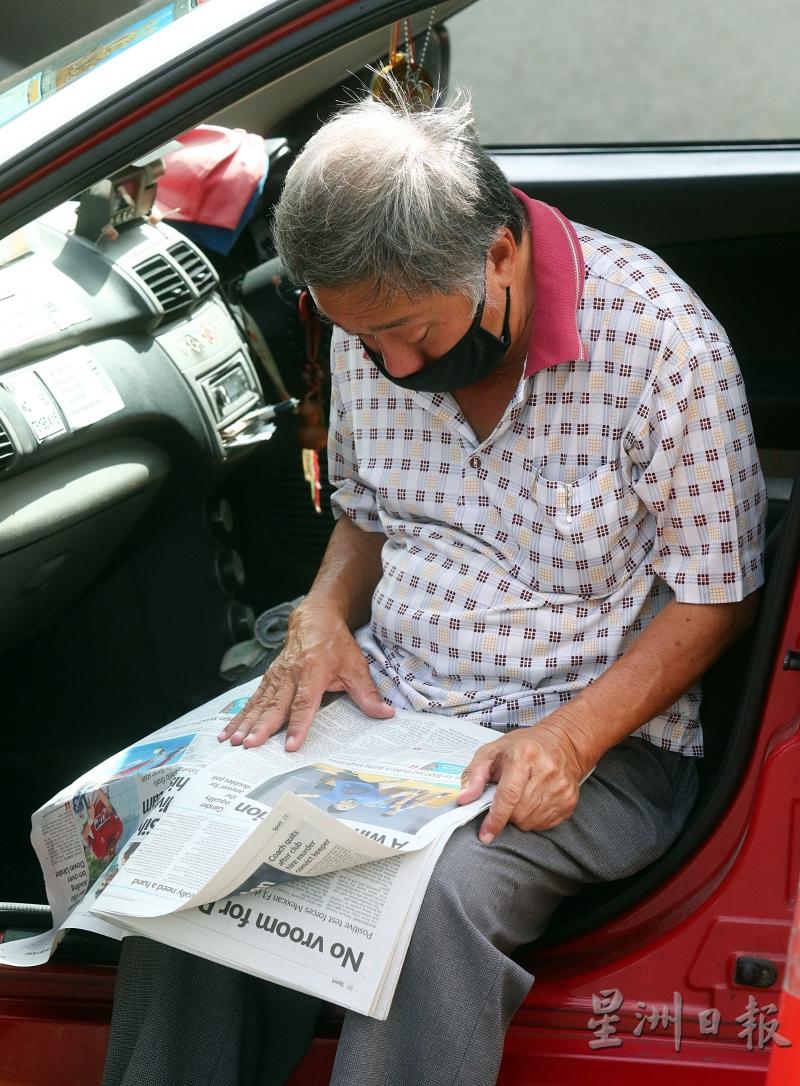 一名戴着口罩的德士司机在等顾客的当儿，看报纸消磨时间。

