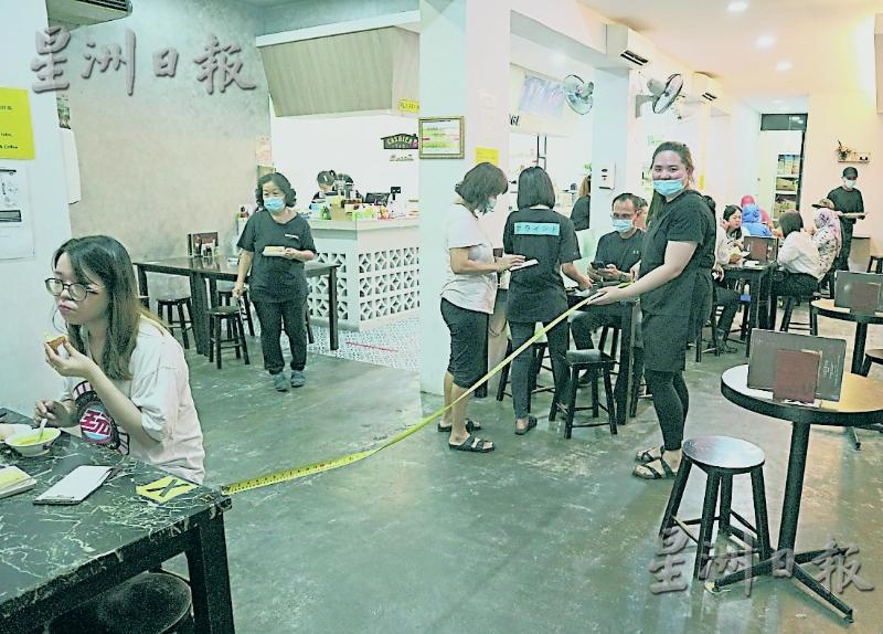 随著政府收紧标准作业程序，餐厅业者在店内进行测量工作，确保桌子之间的距离符合标准。
