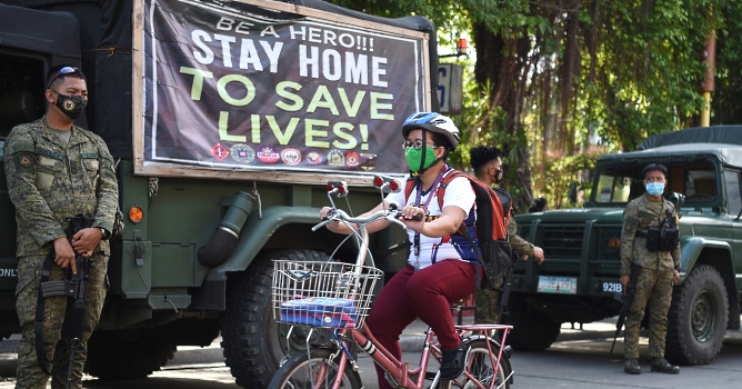 A resident rides cycles past armed soldiers along a street in Navotas in suburban Manila. AFP