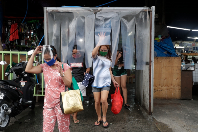 菲律宾总统杜特尔特在首都马尼拉和周边省份实施封锁措施，奎松市是其中一个，图示妇女在公共市场购买食物后离开消毒区。（美联社照片）