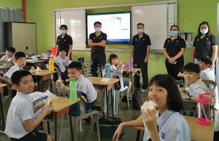麻坡中华基小营养餐计划开跑,学生在课室内用餐,黄荣强(后排左二)及多位老师前往视察。 麻坡中华基小营养餐计划开跑,学生在课室内用餐,黄荣强(后排左二)及多位老师前往视察。