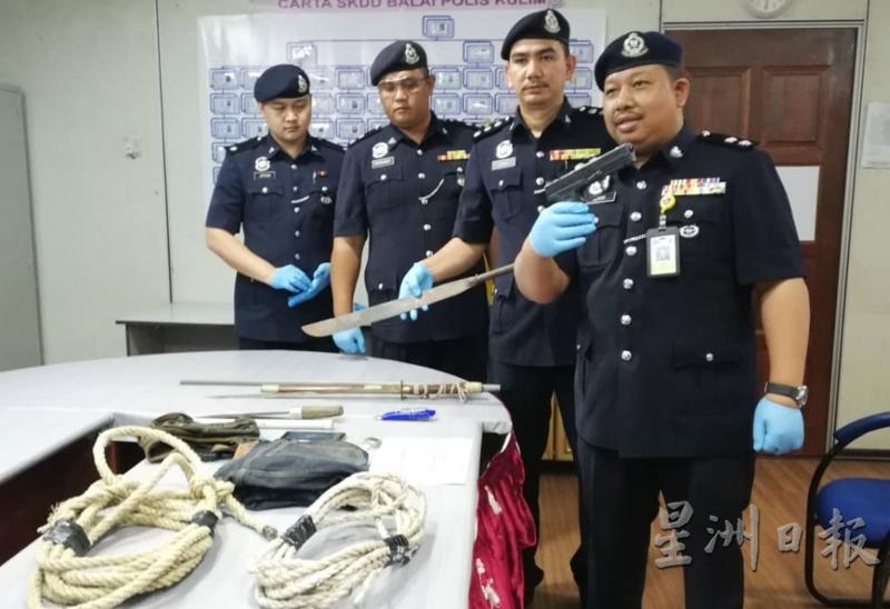 阿兹哈（右一）在众警官的陪同下展示起获的物件，包括1把假枪。

