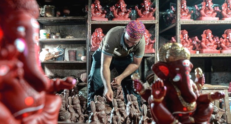 Muslim potter Yusuf Zakaria Galwani inspects a clay idol of elephant-headed Hindu god Ganesha at his workshop inside the Dharavi slum in Mumbai. AFP