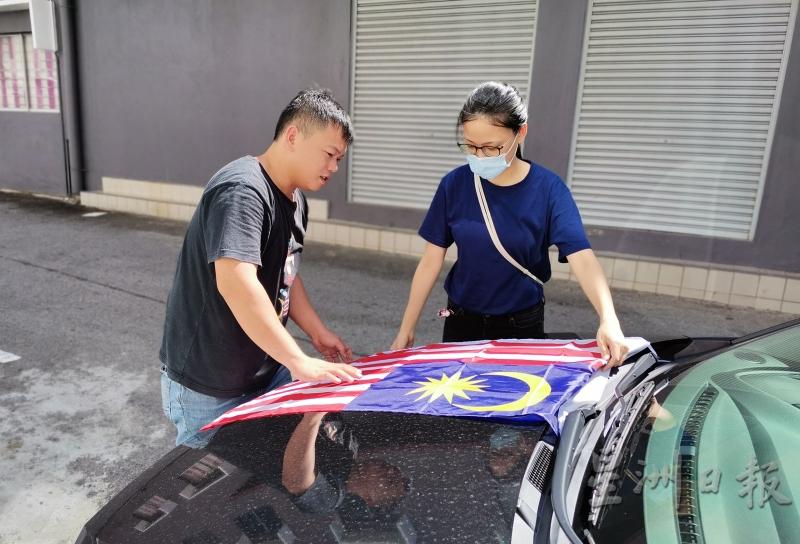 叶文意（右）在同事协助下，将国旗贴在轿车，准备迎接国庆。