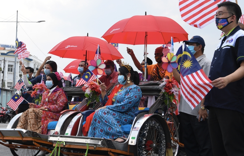 槟城民众身穿民族传统服装，骑着三轮车挥舞辉煌条纹欢庆国庆日。（马新社照片）