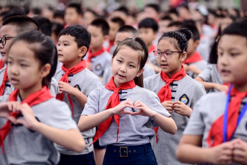 小学生在开学升旗礼比出爱心手势，感谢在抗疫奋战的前线人员。
