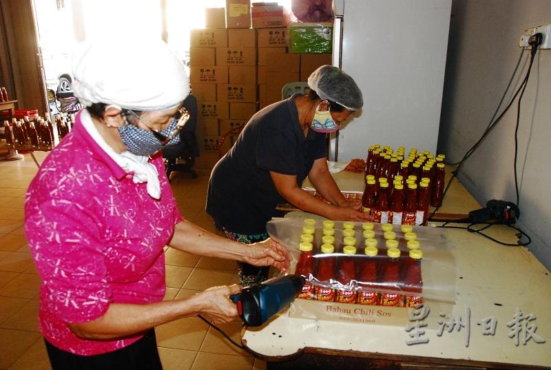 邹梅芳和工人利用吹风筒，将辣椒酱包装起来。