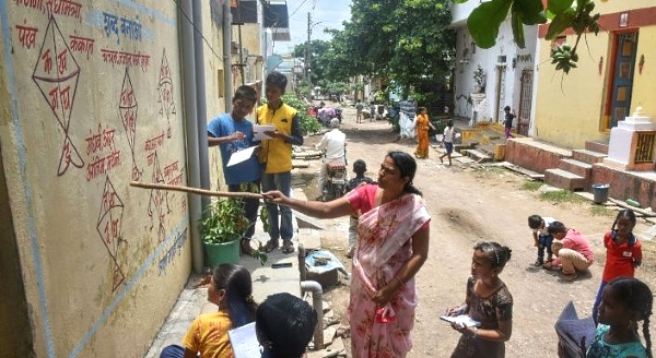 A teacher in Nilamnagar village points to a writing from textbooks painted on the wall of a house to teach students unable to attend online classes during the pandemic. AFP A teacher in Nilamnagar village points to a writing from textbooks painted on the wall of a house to teach students unable to attend online classes during the pandemic. AFP