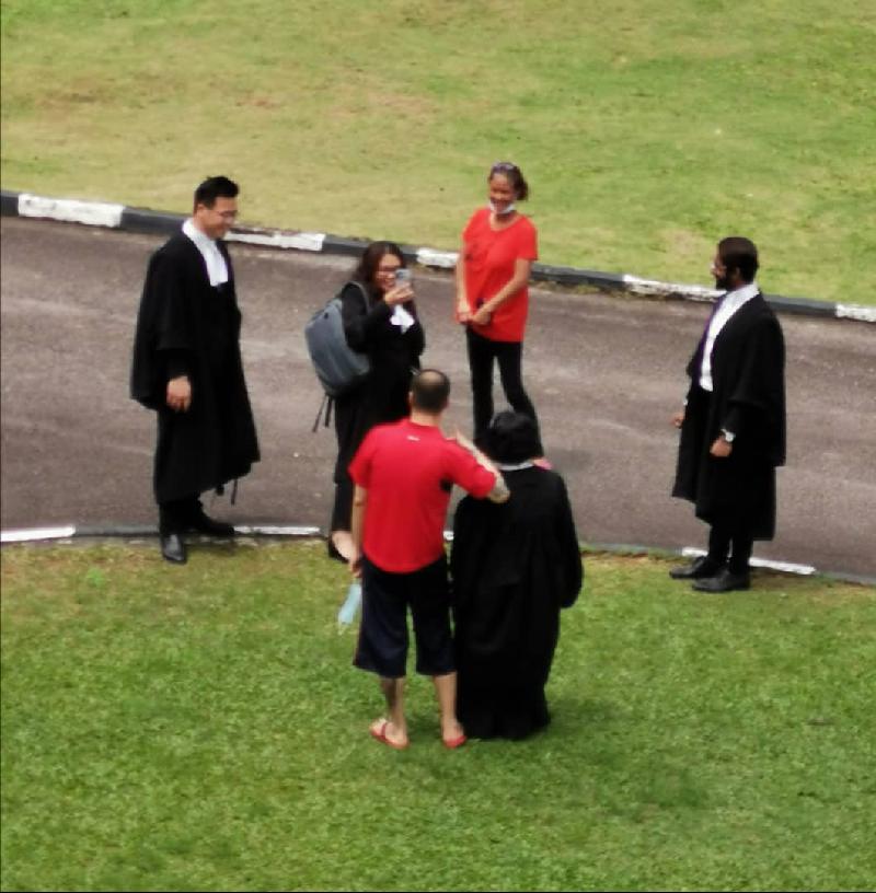 第一被告颜嘉杰（背对镜头左一）在庭外换上红色汗衫后，欣喜与代表律师合照。
