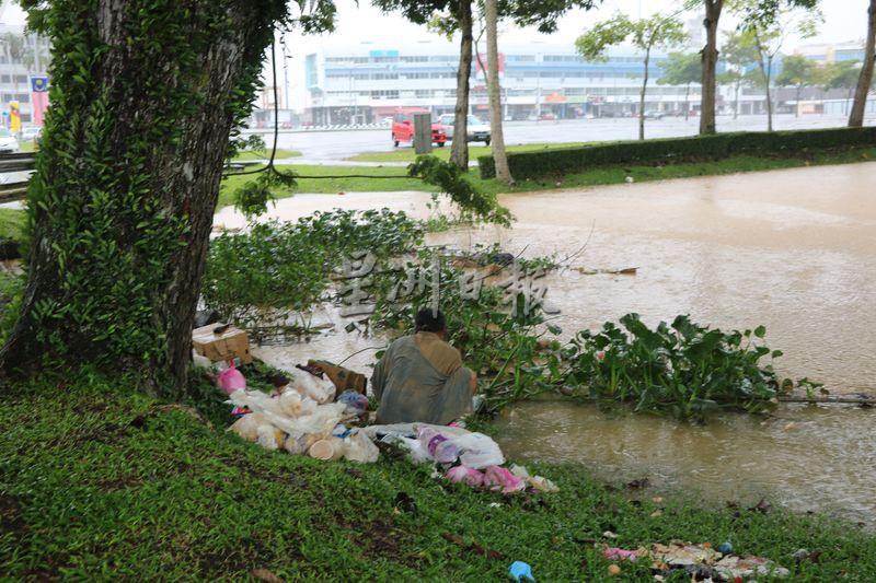 虽然树下已淹水，但中年流浪汉，不离开，冒雨在垃圾堆中觅食。
