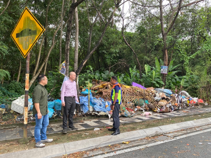 林立迎（中）和固体废料及卫生管理机构官员巡视大路边树林旁的非法垃圾堆。左为游佳豪。