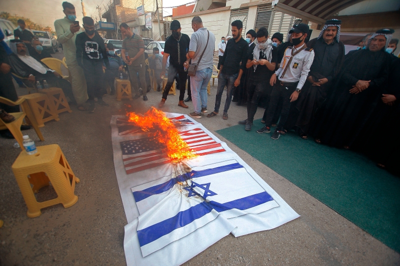 伊朗的伊拉克民兵组织支持者焚烧美国、英国和以色列的国旗。（图：美联社）