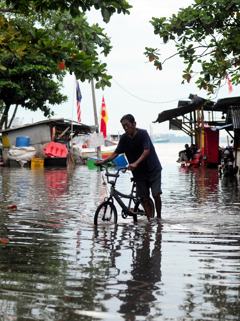 巴生港口海南村于上午时分被海水淹上的一幕，一名居民无奈推着脚踏车徐徐走过。（马新社）